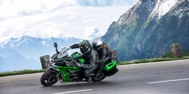 Twee motorrijders sturen een groene toermotor door een bergbocht